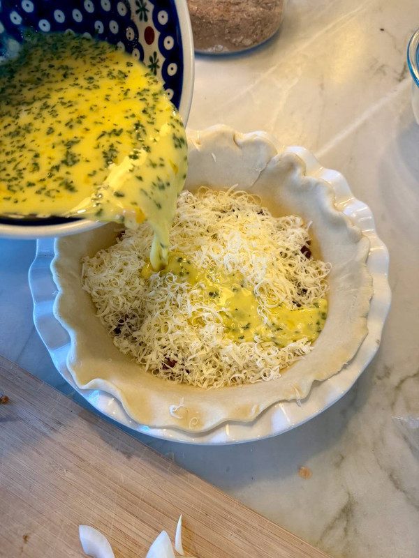 Egg and cream poured over grated cheese in a pie crust