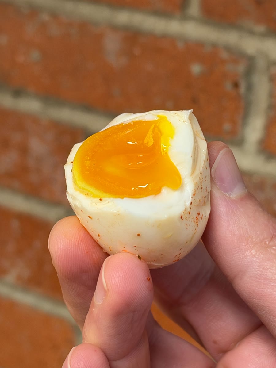 A soft-boiled egg bitten open to a jammy orange yolk, dusted with paprika
